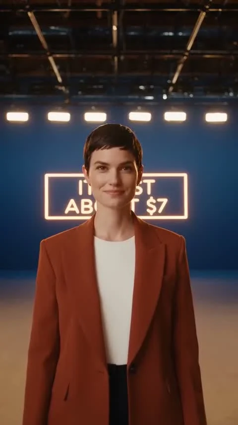 Final seconds of the same 30-second single take: the character stops in front of a neon sign the model generated with legible dollar-amount text, identity held from the first frame